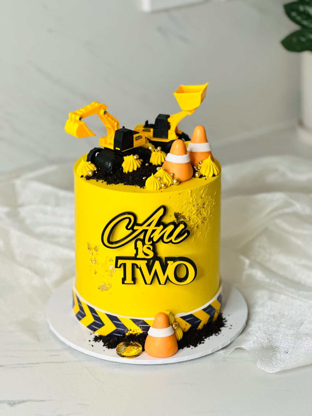 Construction cake in yellow buttercream with toy excavator, front loader, traffic cones and Oreo crumb 'dirt' — CCT Sydney