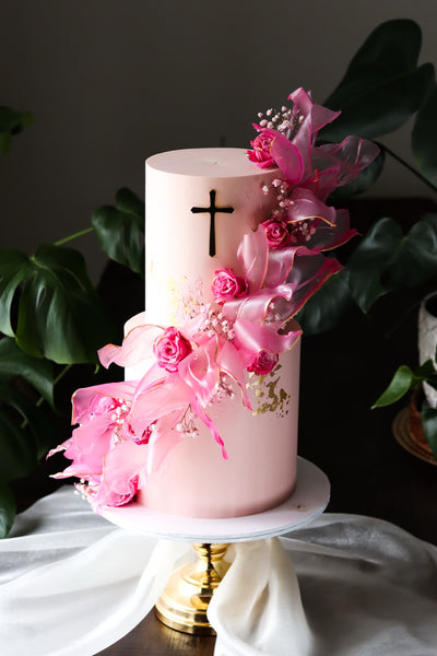 Two tier pale pink baptism cake with a gold cross, magenta ruffled sails and gold leaf detail