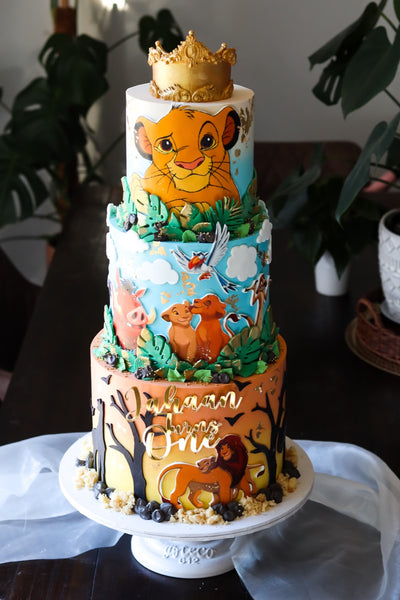 Three tier jungle themed first birthday cake with hand-painted animals and a gold crown topper