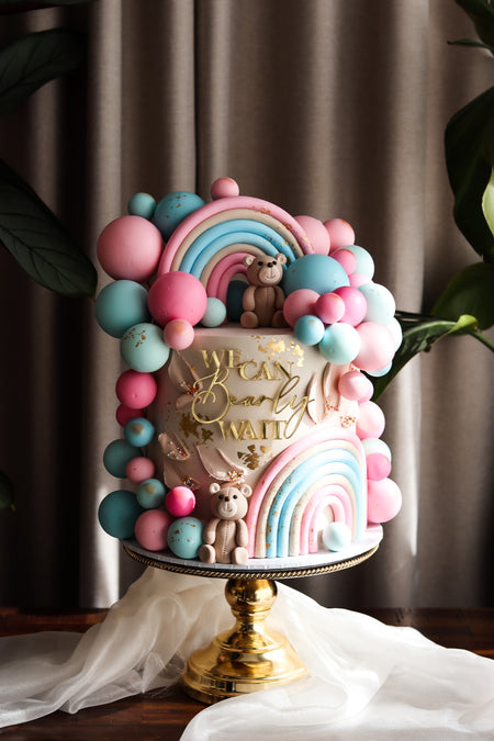 Pastel baby shower cake with a fondant rainbow, balloon garland and teddy bear topper