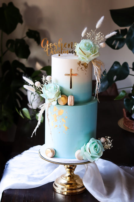 Two-tier mint and blue ombre christening cake with a gold cross, dried florals and macarons