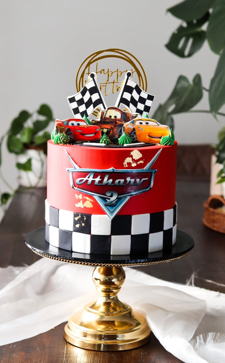 Red race car themed birthday cake with chequered flag detail and modelled car toppers