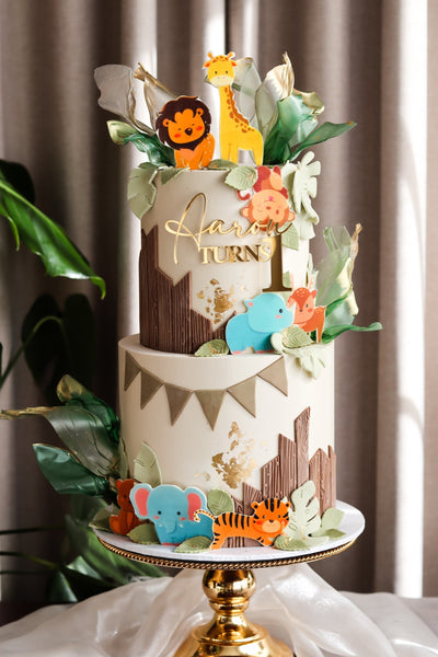 Two tier safari themed first birthday cake with jungle animal toppers, bunting and foliage