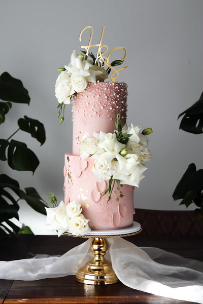 Two tier pink and white wedding cake with pearl beading, fresh white roses and a gold monogram