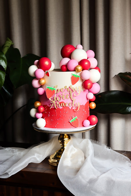 Red and pink strawberry themed birthday cake with a balloon garland