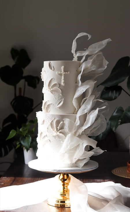 Two-tier white baptism cake with textured sugar ruffles and a piped cross