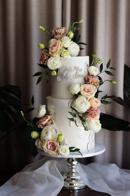 Two-tier white wedding cake with cascading blush and ivory roses