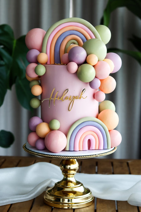 Pastel pink birthday cake with a fondant rainbow and pastel balloon garland