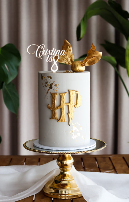 White buttercream cake with a gold fondant monogram and gilded sugar wings