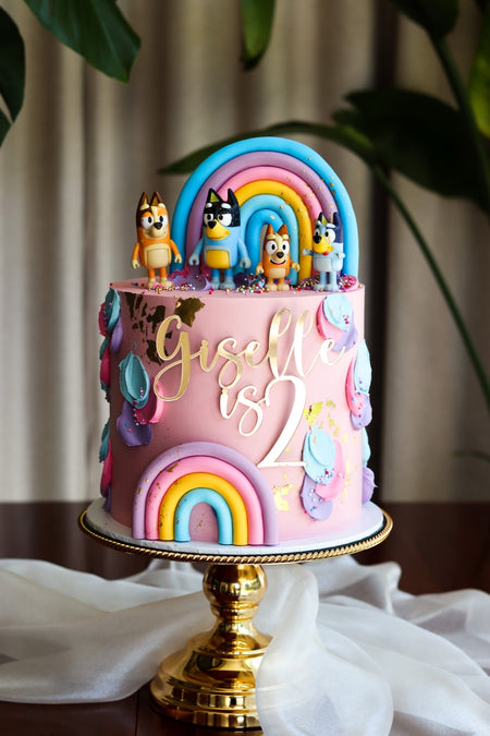 Pink birthday cake with cartoon dog toppers and a fondant rainbow