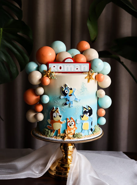 Blue beach themed birthday cake with cartoon toppers, starfish and a balloon garland