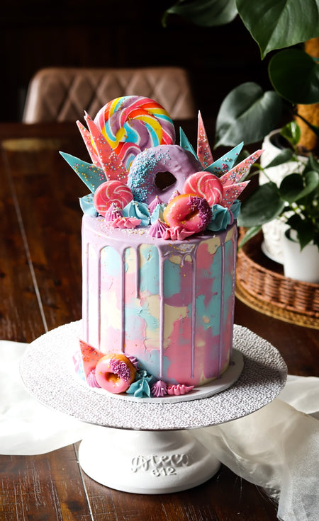 Pastel drip cake topped with lollipops, doughnuts and meringue shards