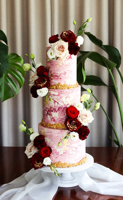 Three tier pink marbled cake with burgundy and ivory roses and gold banding