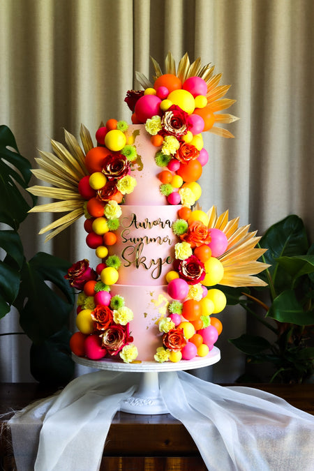 Three-tier pink and orange tropical cake with sugar flowers and gold palm fans
