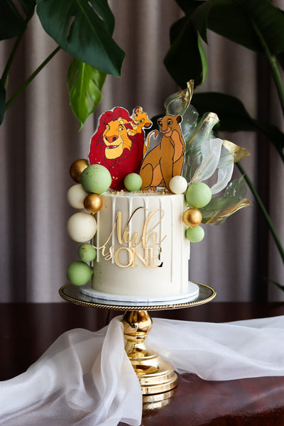 Single tier jungle themed first birthday cake with hand-cut animal toppers and a pastel balloon garland
