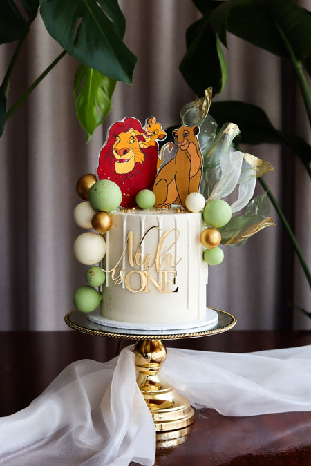 Jungle themed first birthday cake with hand-cut animal toppers and a pastel balloon garland