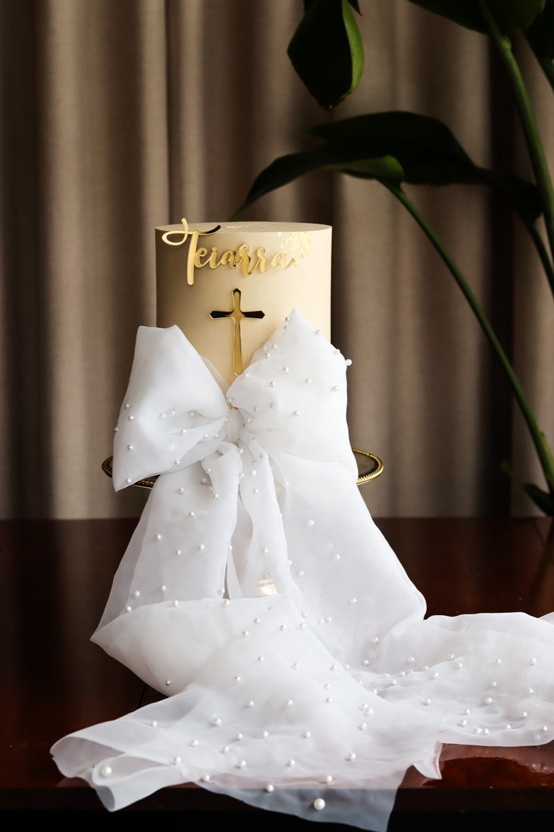 Ivory baptism cake with an oversized pearl-studded organza bow