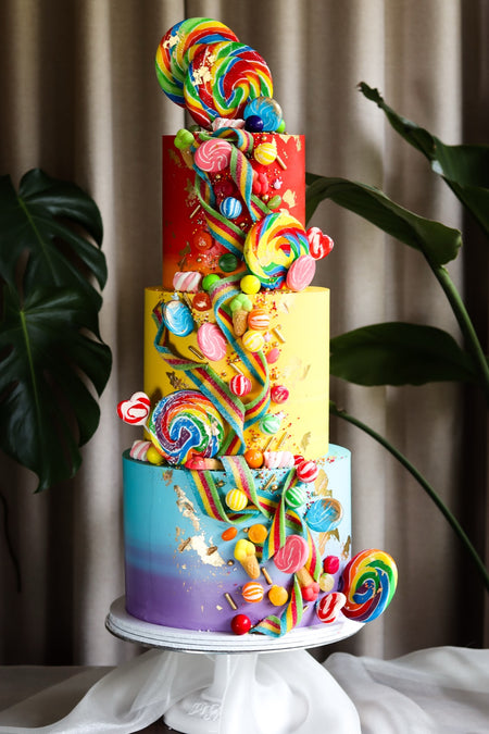 Three-tier rainbow candy cake with lollipops, swirls and bright buttercream