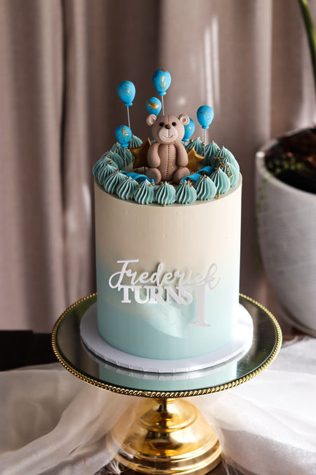 Mint and cream first birthday cake with a modelled teddy bear and balloon toppers