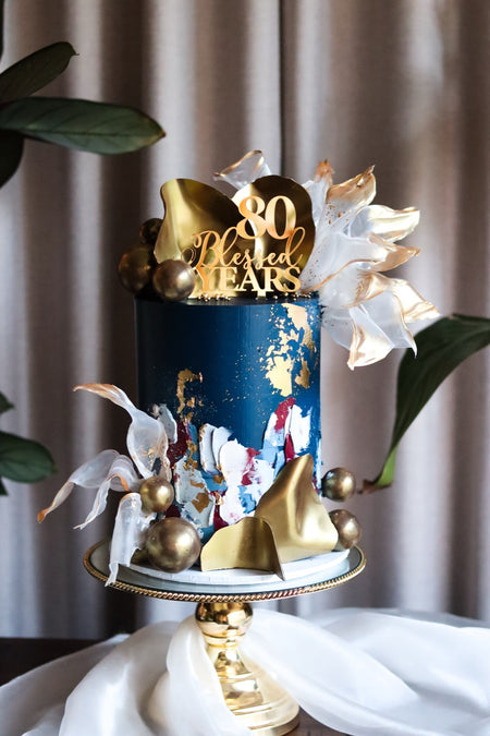 Navy and gold 80th birthday cake with gold leaf, sails and sugar shards