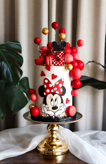 Red and white polka dot third birthday cake with a cartoon mouse topper and balloon garland