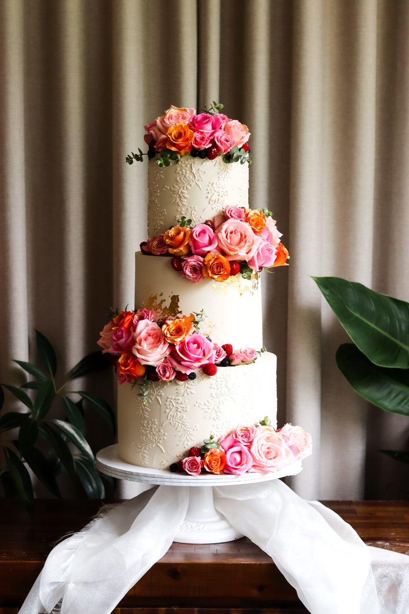 Three-tier white wedding cake with fresh pink and orange roses