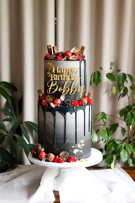 Black chocolate drip cake loaded with chocolate bars, truffles and strawberries