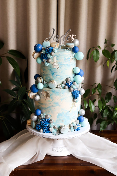 Two-tier blue and silver cake with sugar shells, pearls and a marbled finish
