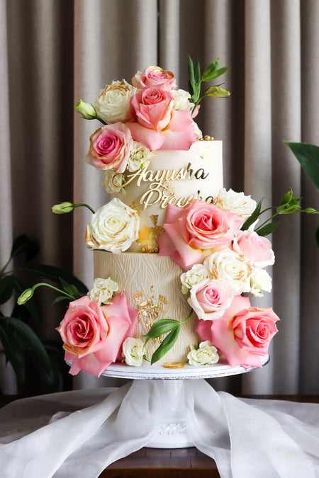 Two-tier ivory cake with pink and white fresh roses and gold leaf detail